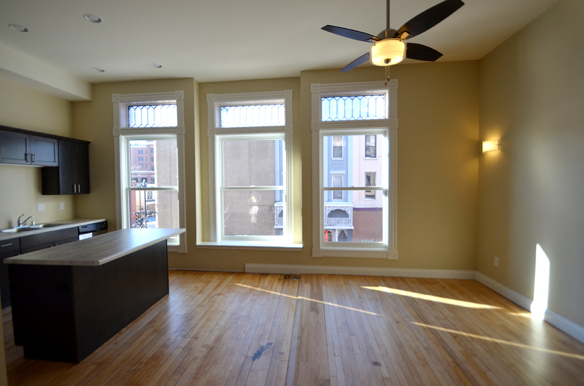 an empty living room with a ceiling fan and large windows