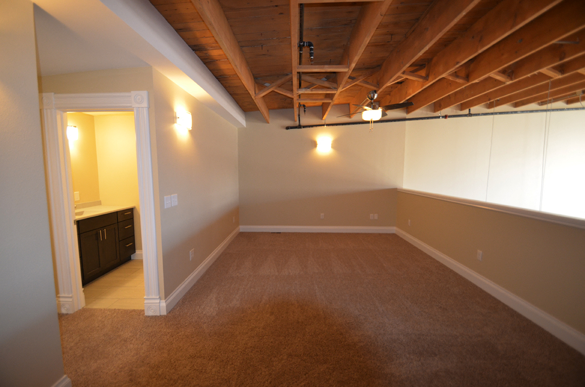 an empty living room with a carpeted floor and exposed wood ceilings