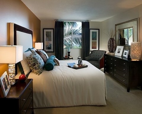A bedroom with a large bed, a nightstand with a lamp, and a dresser with a mirror.