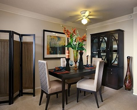 A dining room with a table, chairs, and a vase of flowers.