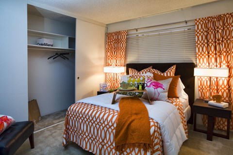 A bedroom with a bed covered in an orange and white patterned comforter and a small table beside it.