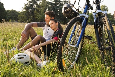 a man and woman sitting in the grass next to a bike