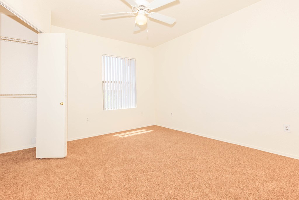 an empty living room with a ceiling fan and a closet