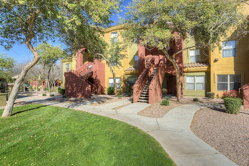 a sidewalk in front of a yellow building with trees