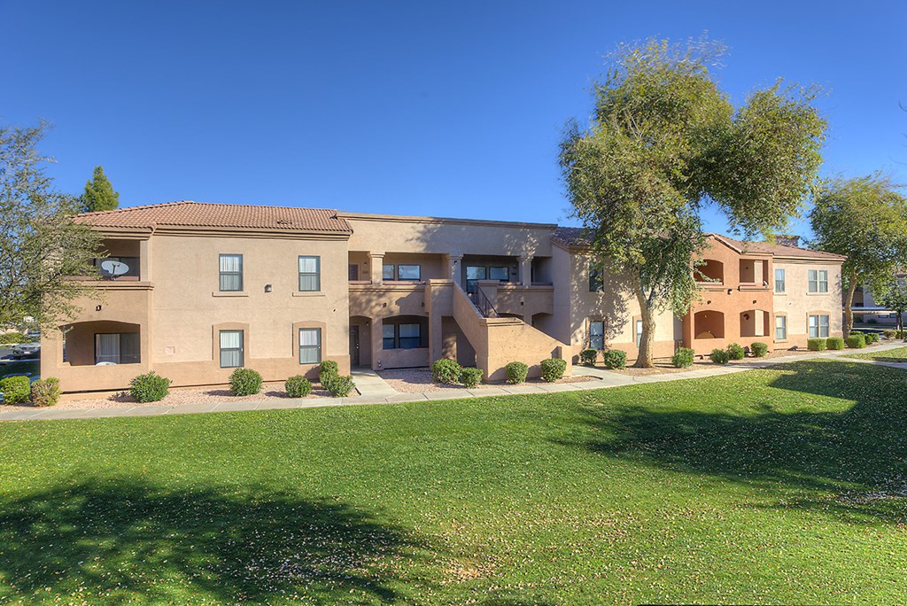 an apartment building with a green lawn and trees