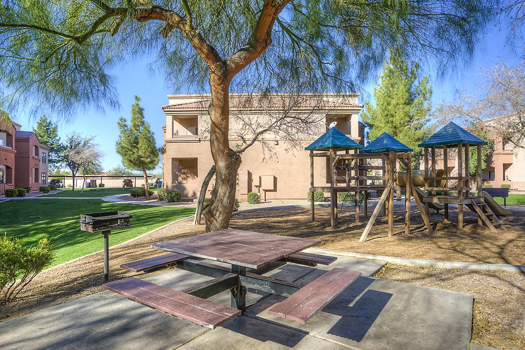 playgrounds and picnic tables under a tree in front of a building
