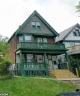 A green house with a porch and a balcony.