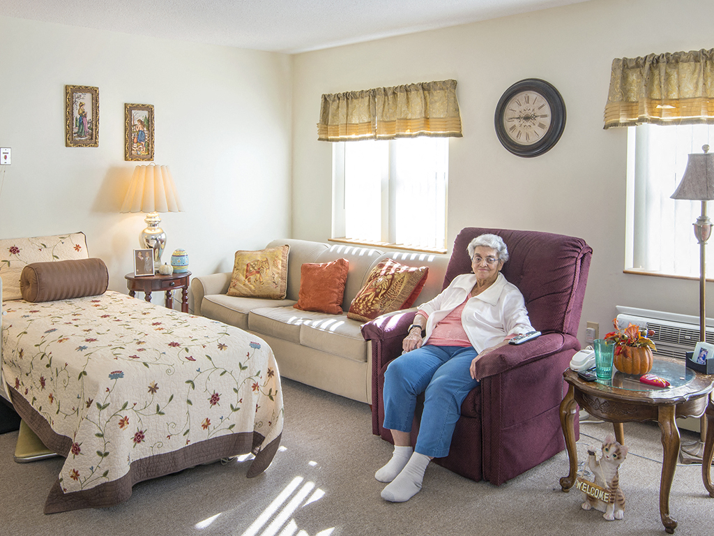 a woman sits in a chair in a living room with a bed