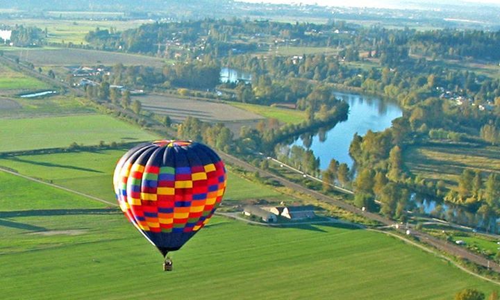 a hot air balloon flying over a field with a river