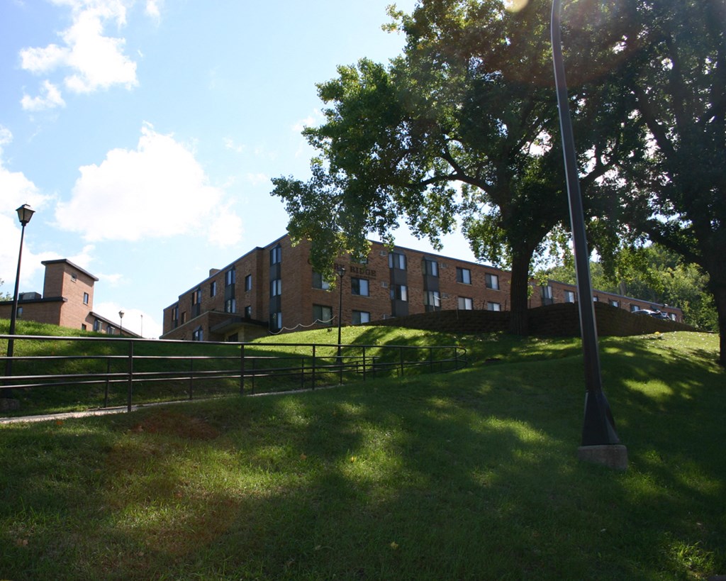 a large brick building on a grassy hill with trees