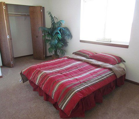 A bed with a red and grey striped comforter sits in a room with a large window and a plant.