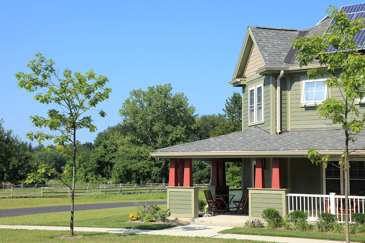 a yellow house with red columns and a white porch with a lawn and trees