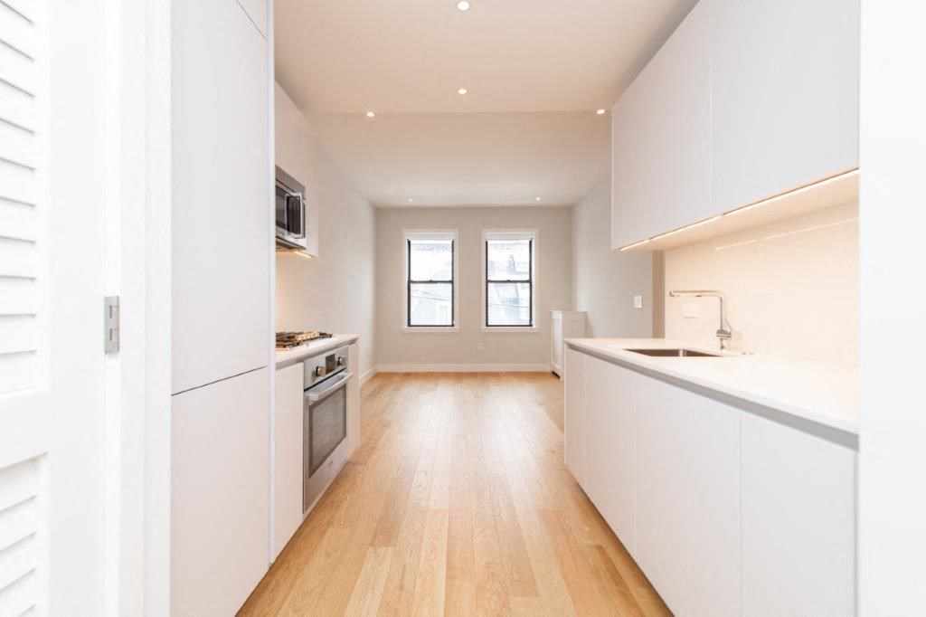 an empty kitchen with white cabinets and a wood floor