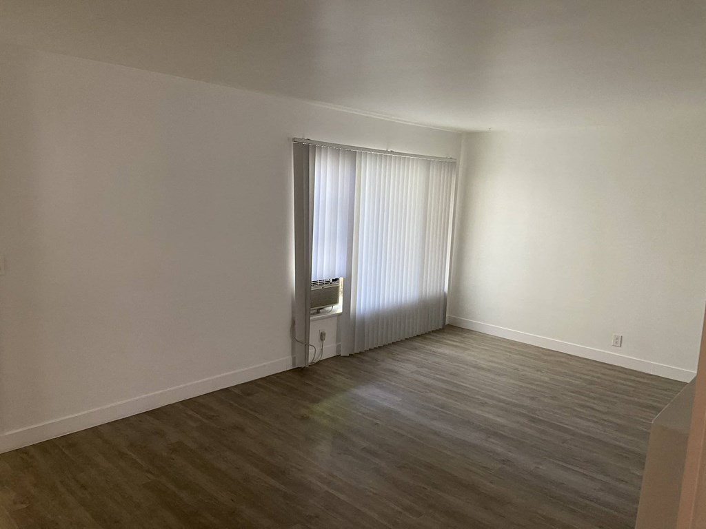 a living room with white walls and wooden floors and a window