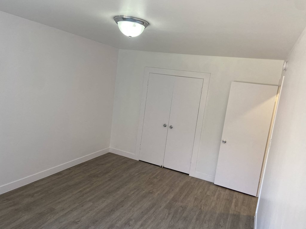 a bedroom with white walls and wood flooring and a closet
