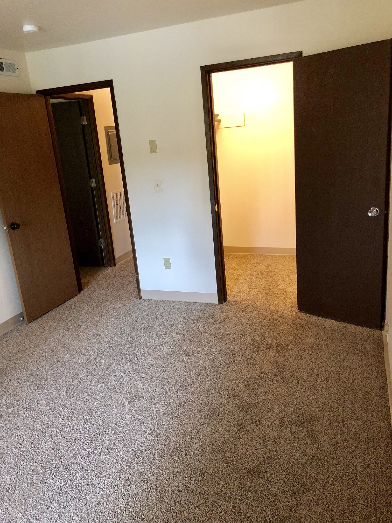 an empty bedroom with three doors and a carpeted floor