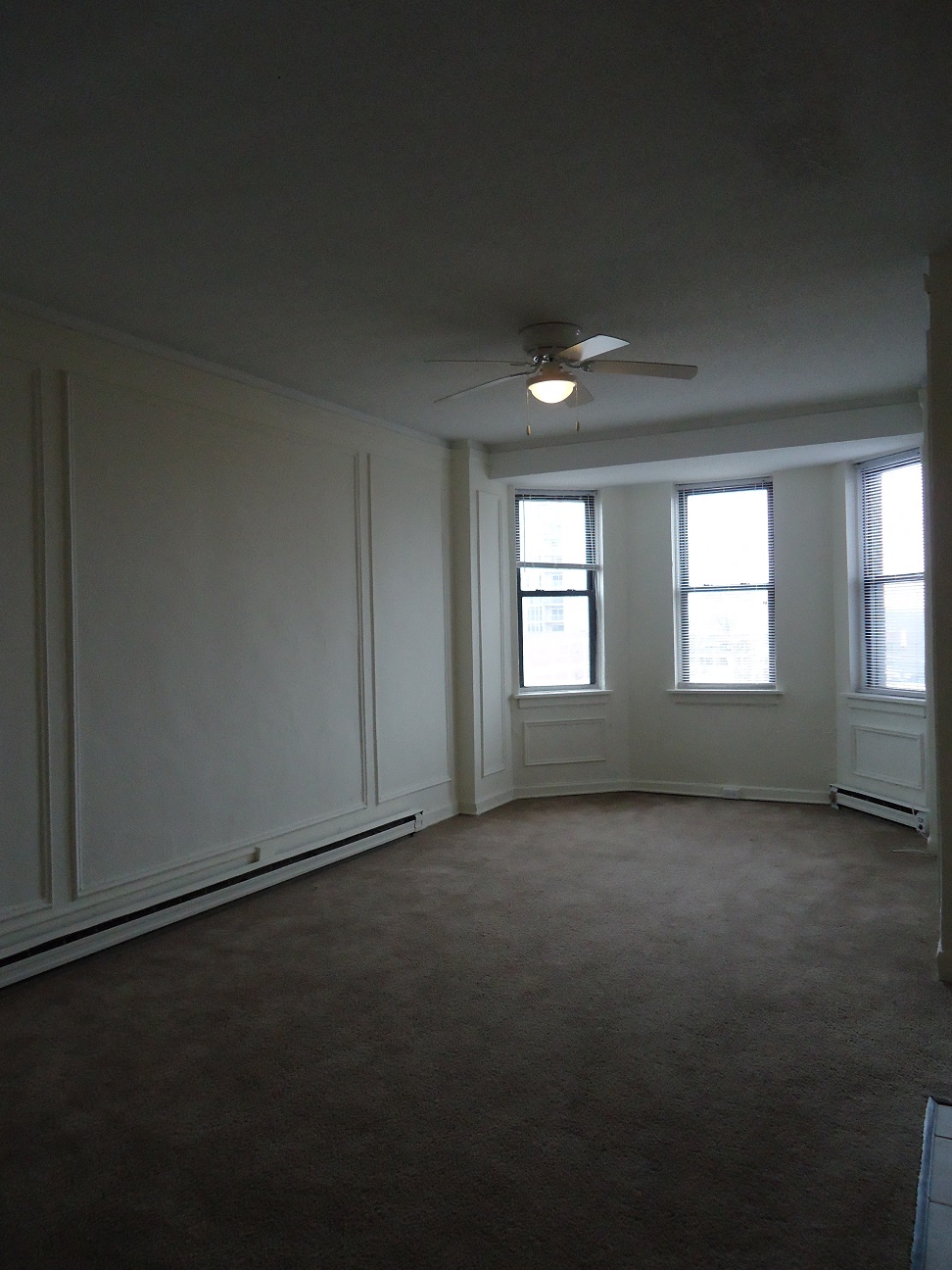 an empty living room with a ceiling fan and three windows