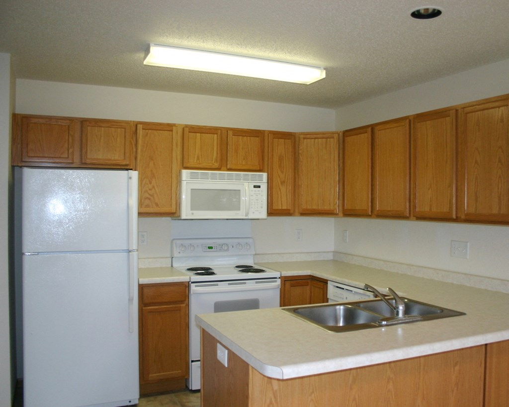 an empty kitchen with white appliances and wooden cabinets
