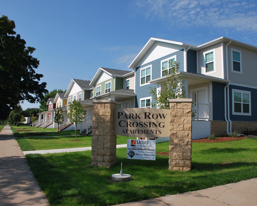 a park row crossing sign in front of a row of houses