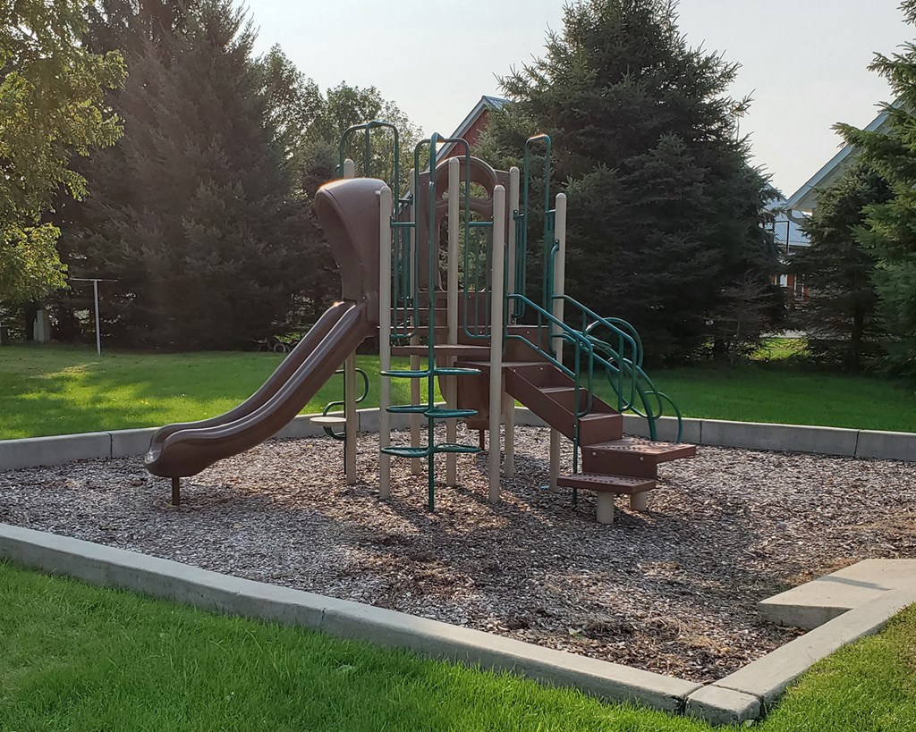A playground with a brown slide and green handrails.