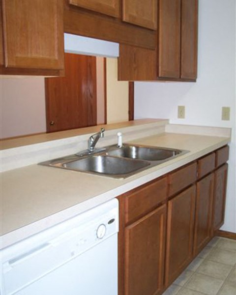 A kitchen with a white dishwasher and brown cabinets.