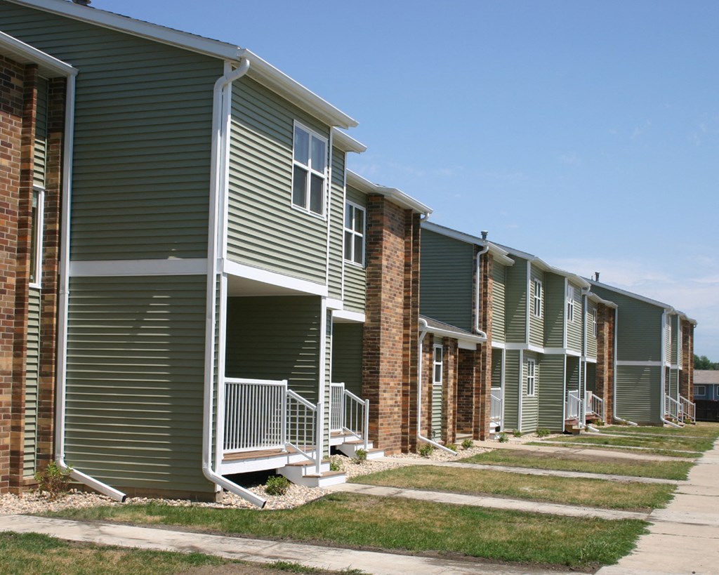 a row of green apartment buildings with stairs and a sidewalk