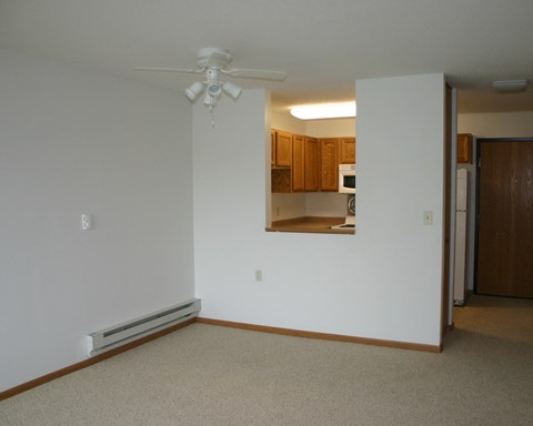 an empty living room with a ceiling fan and a kitchen