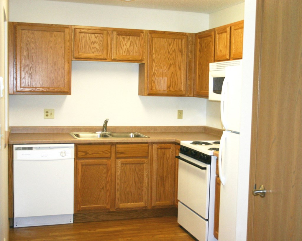 an empty kitchen with white appliances and wooden cabinets