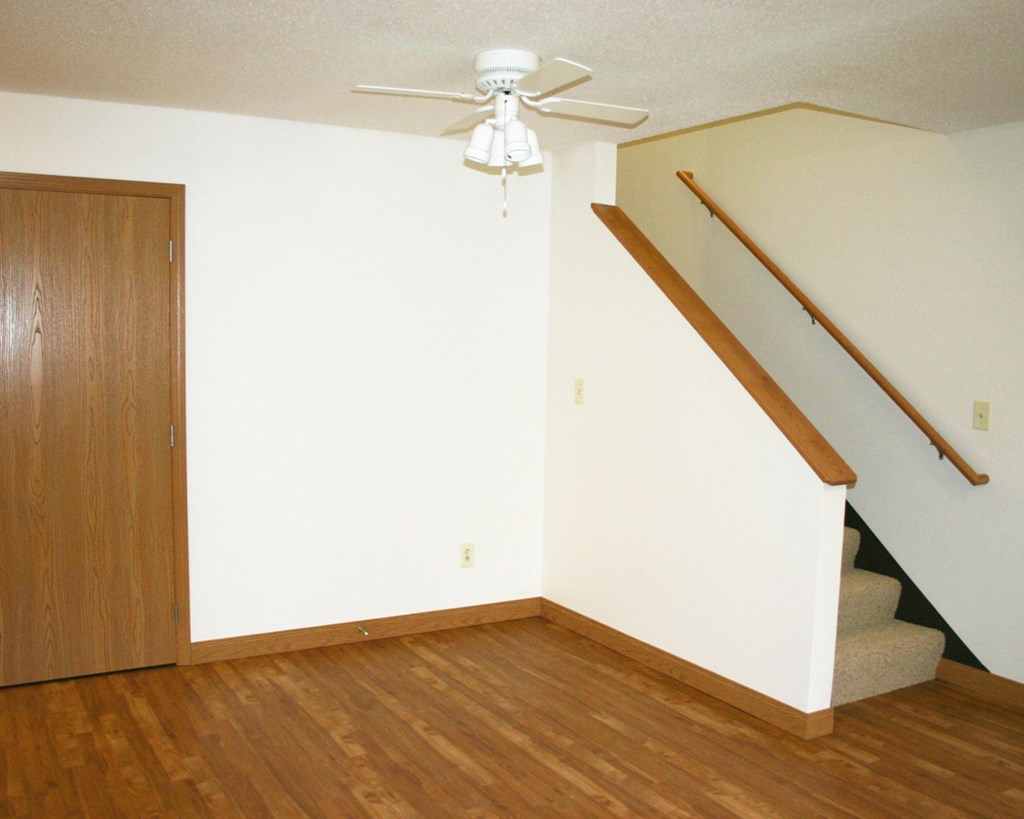 an empty living room with stairs and a ceiling fan