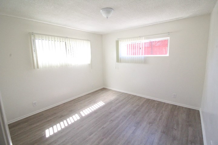 an empty room with wood flooring and two windows
