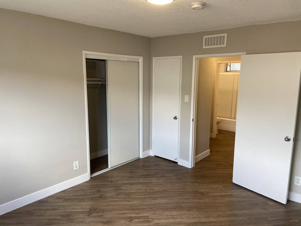 a room with a hard wood floor and a hallway with three doors