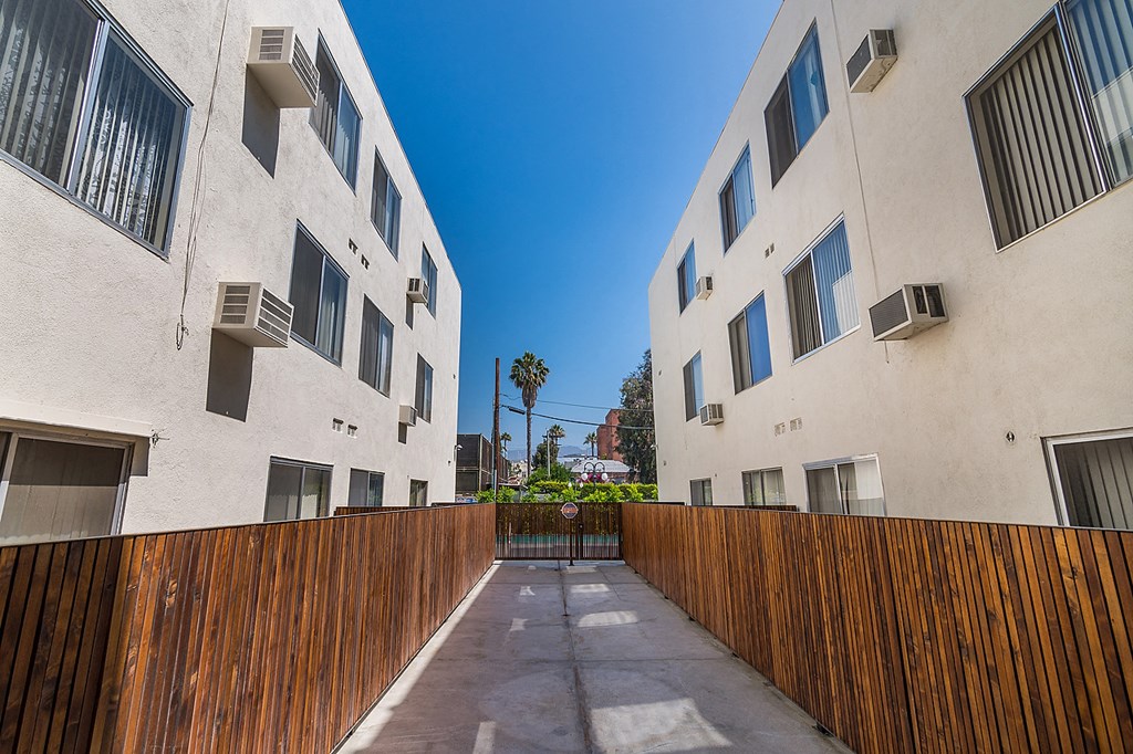 an alley between two apartment buildings with a wooden fence
