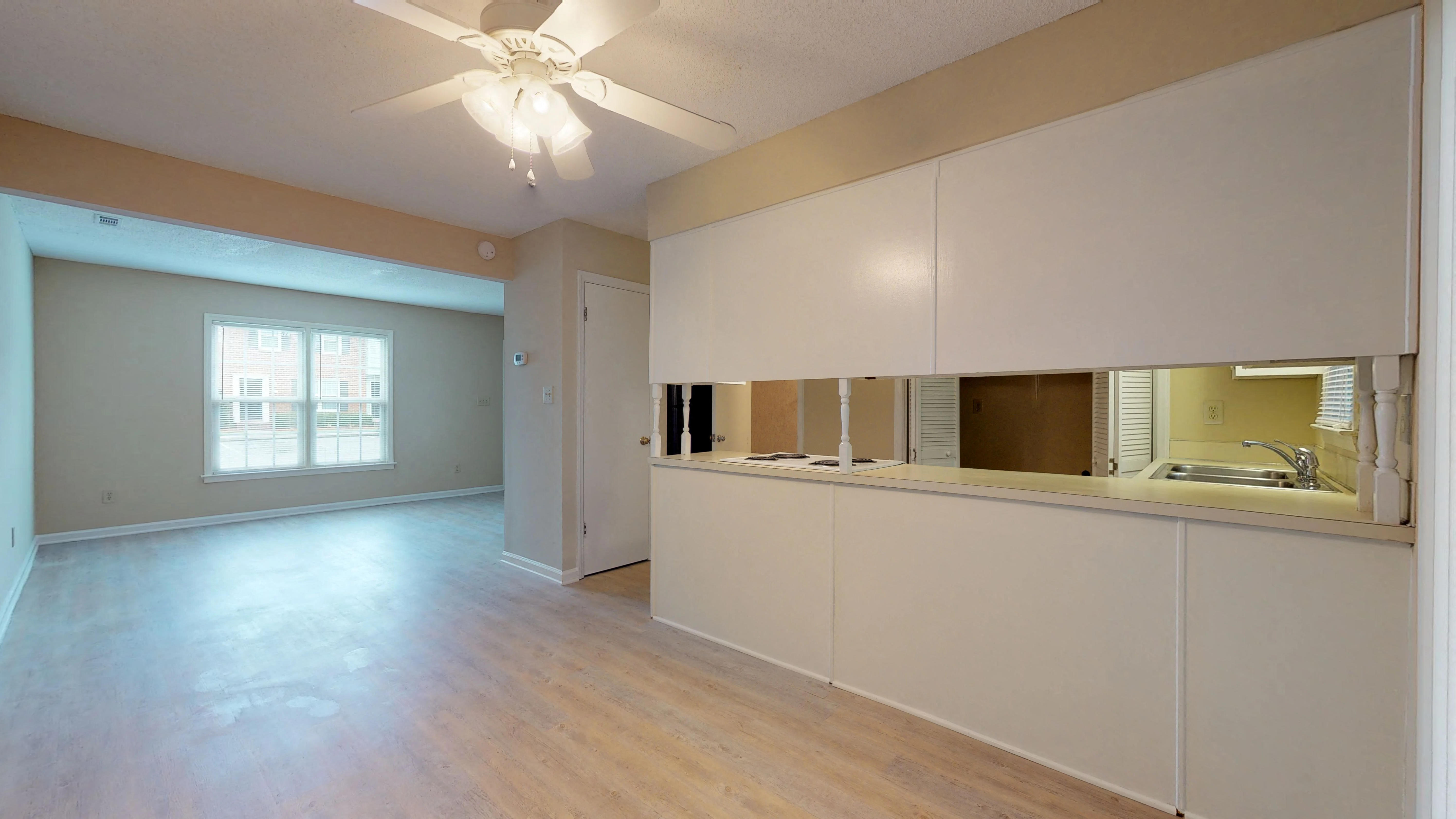 an empty living room with a kitchen and a ceiling fan