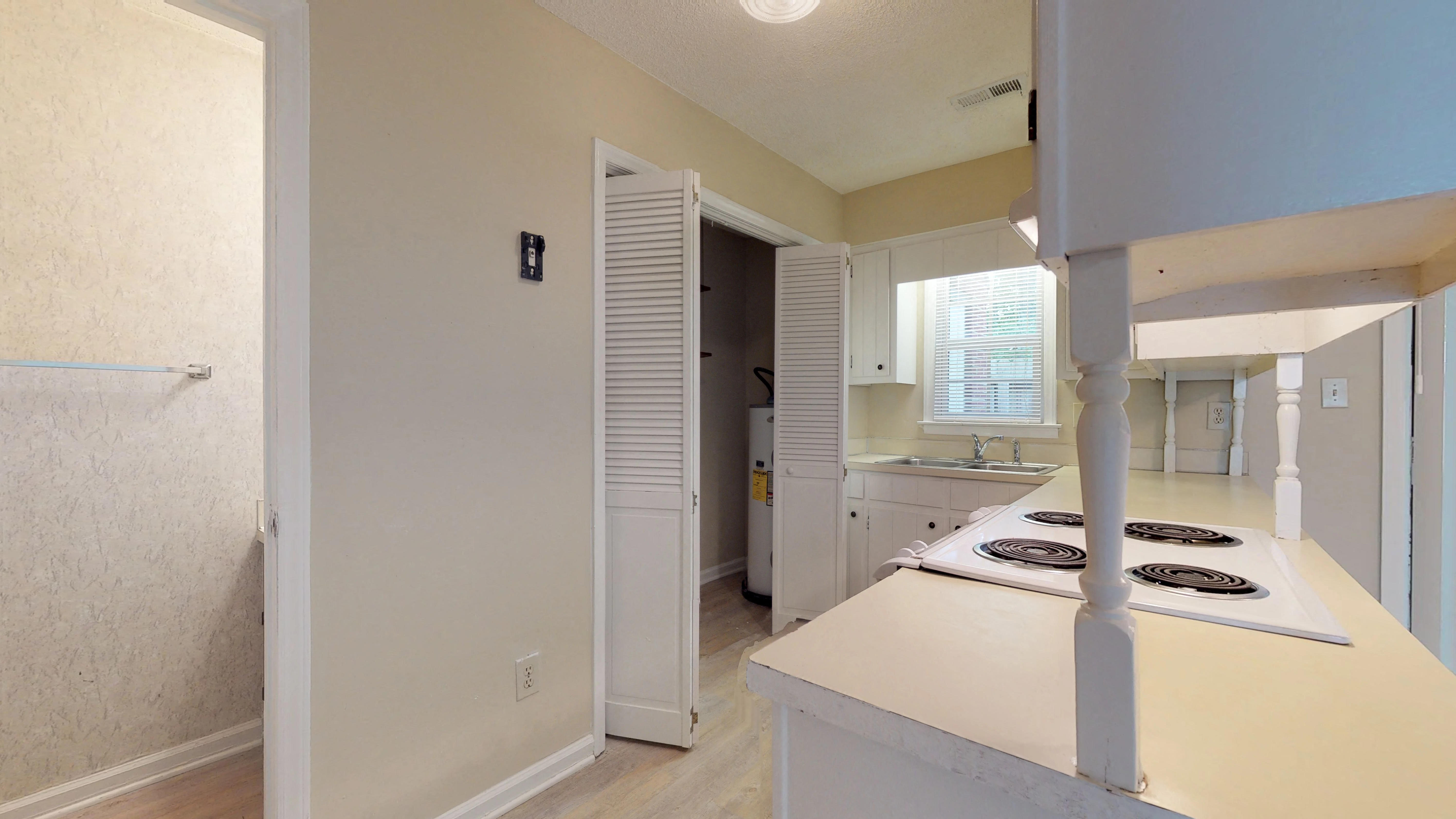 a kitchen with white cabinets and a stove and a hallway to a bathroom