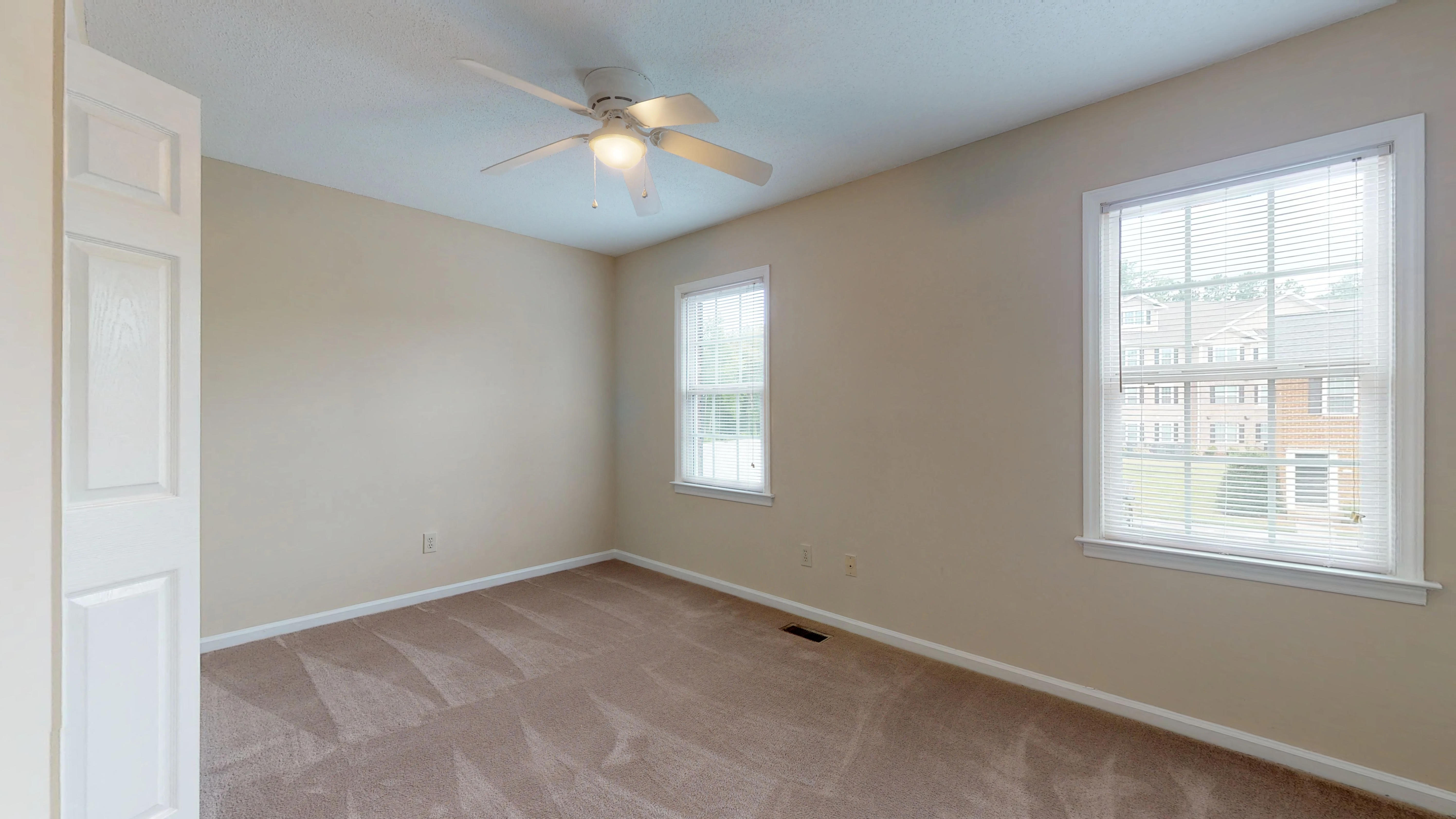 an empty living room with a ceiling fan and two windows