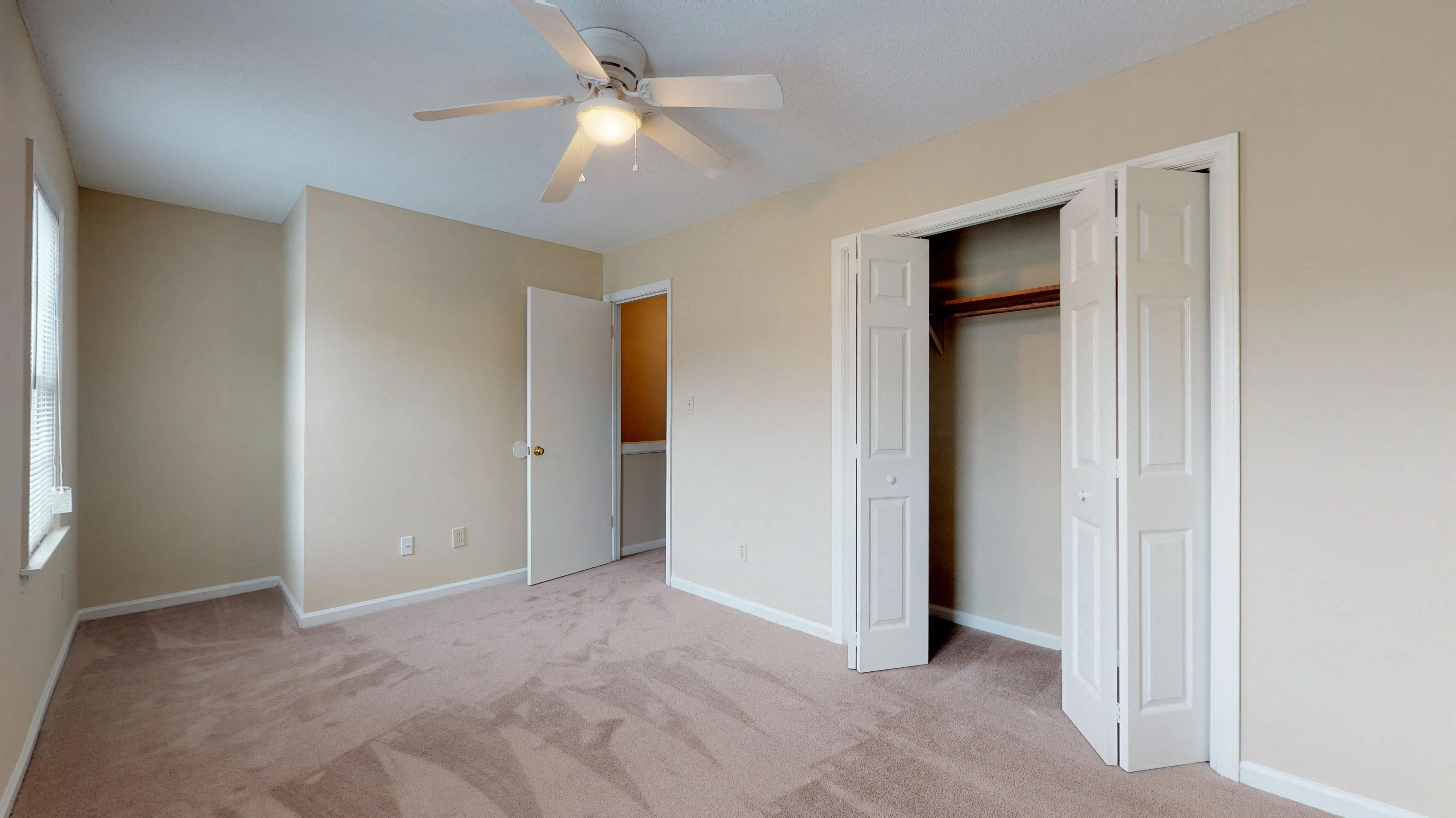 an empty living room with a ceiling fan and a closet