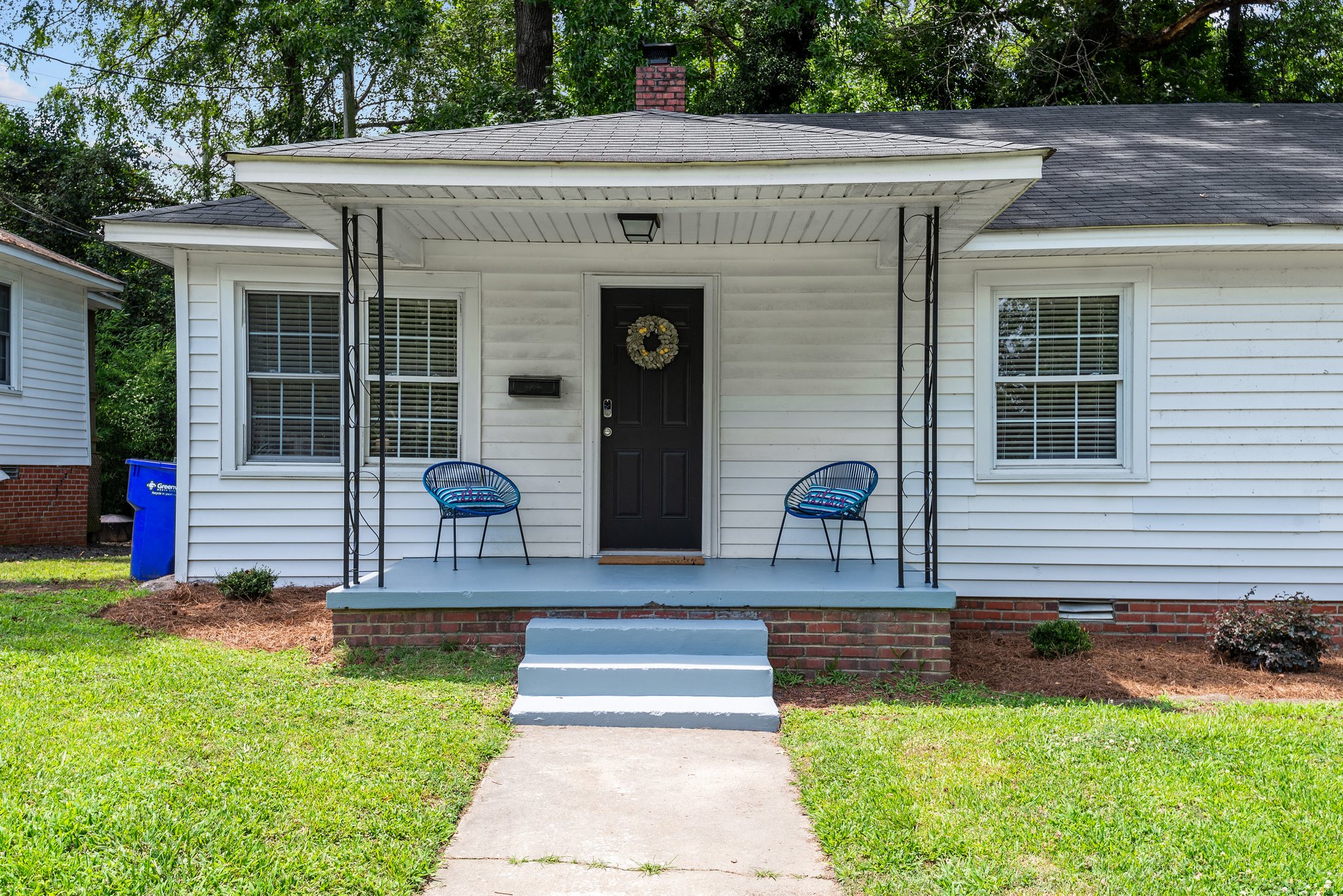the front of a white house with two blue chairs on a porch