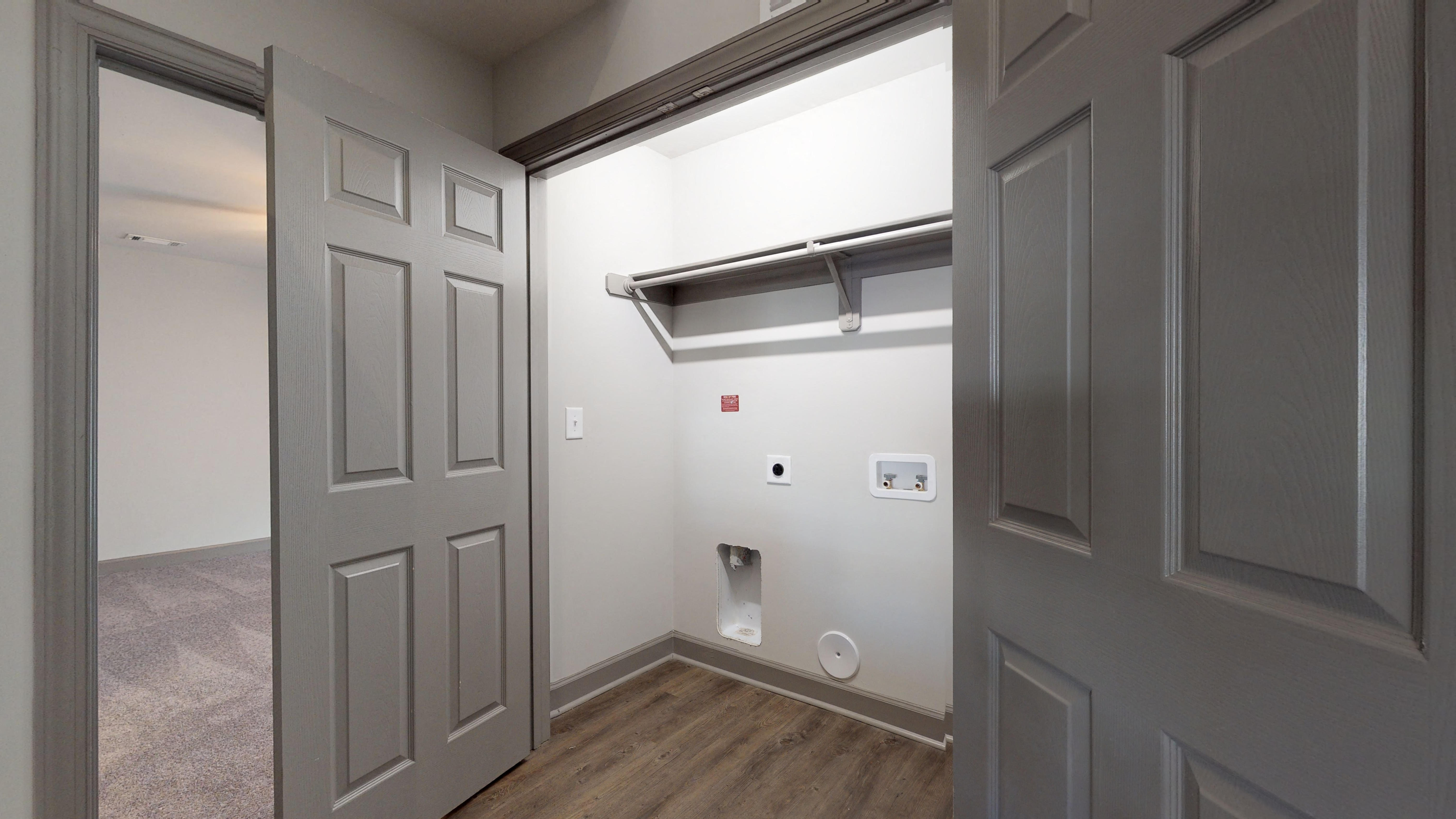 an empty hallway with a door to a room with a toilet and a white wall