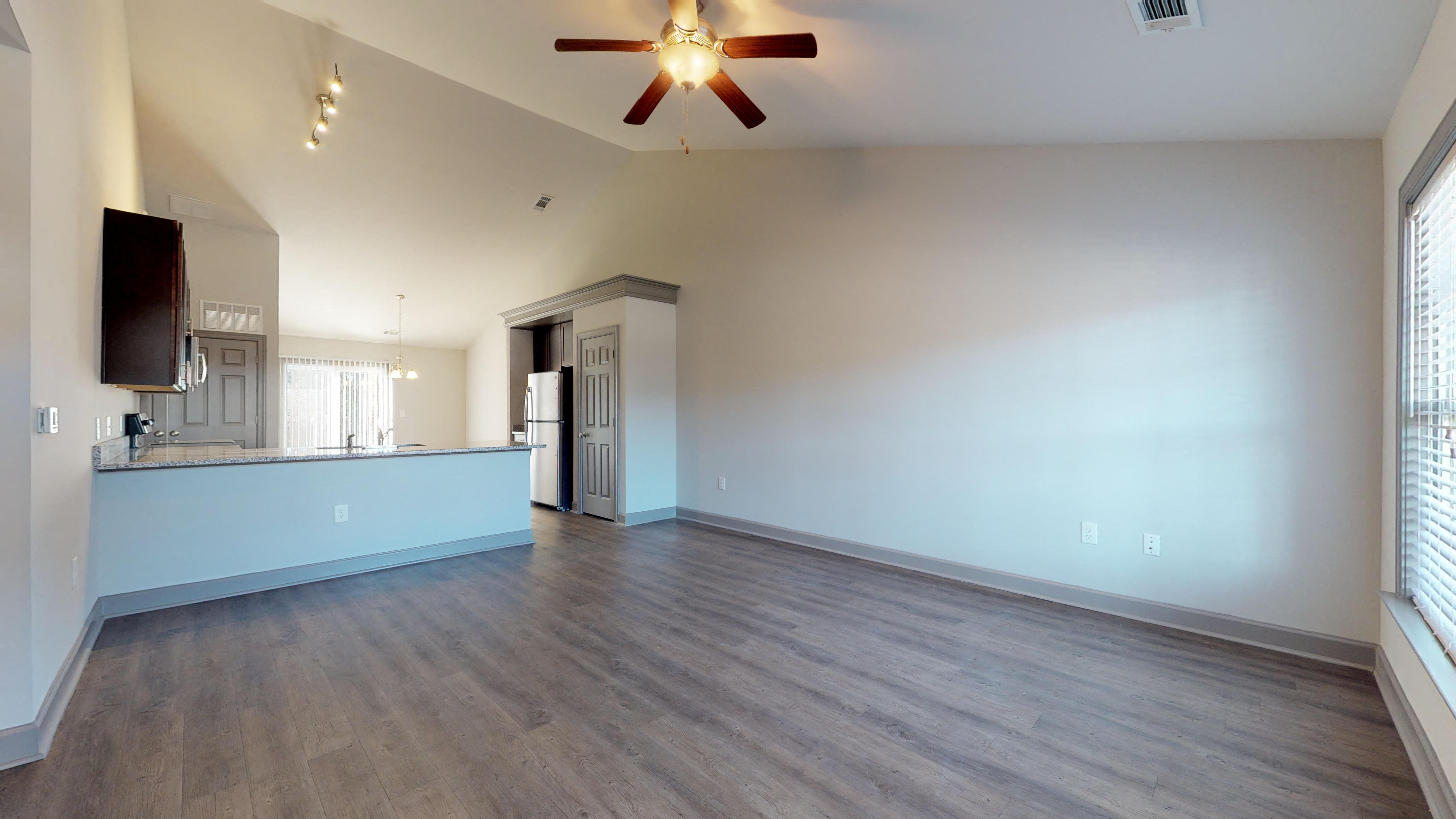 an empty living room with a ceiling fan and a kitchen