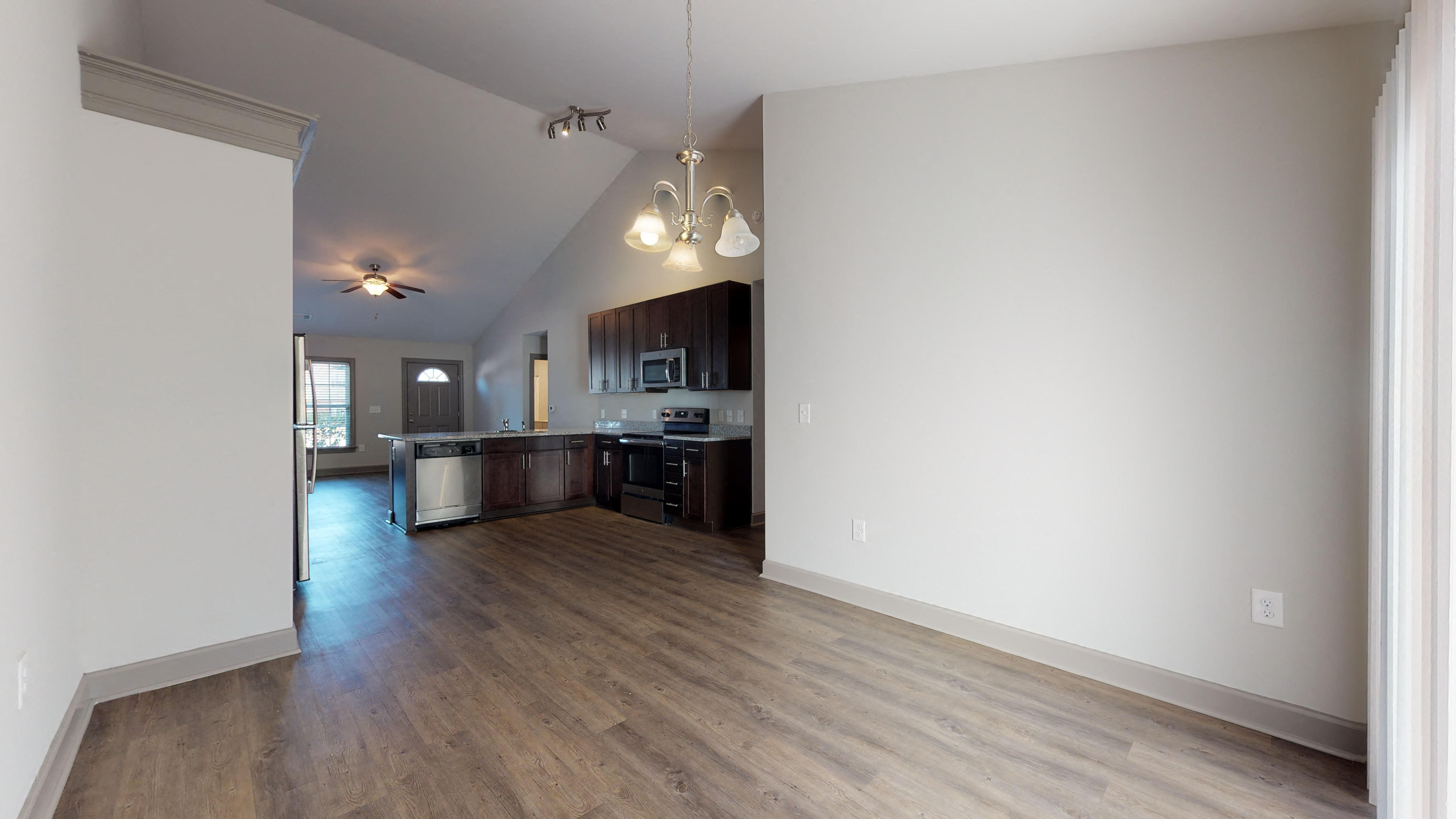 an empty living room and kitchen with wood floors and white walls
