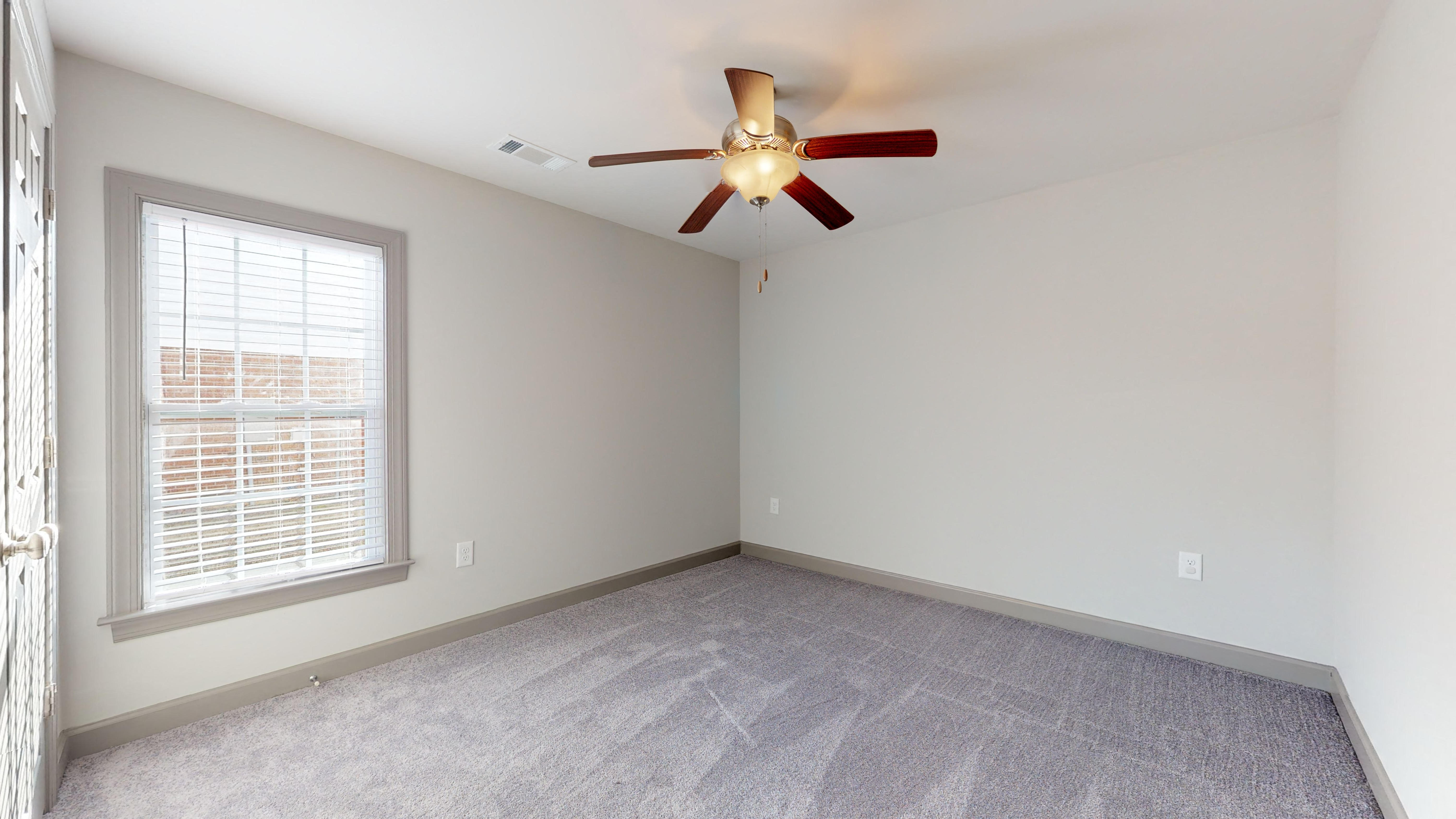 an empty bedroom with a ceiling fan and a window