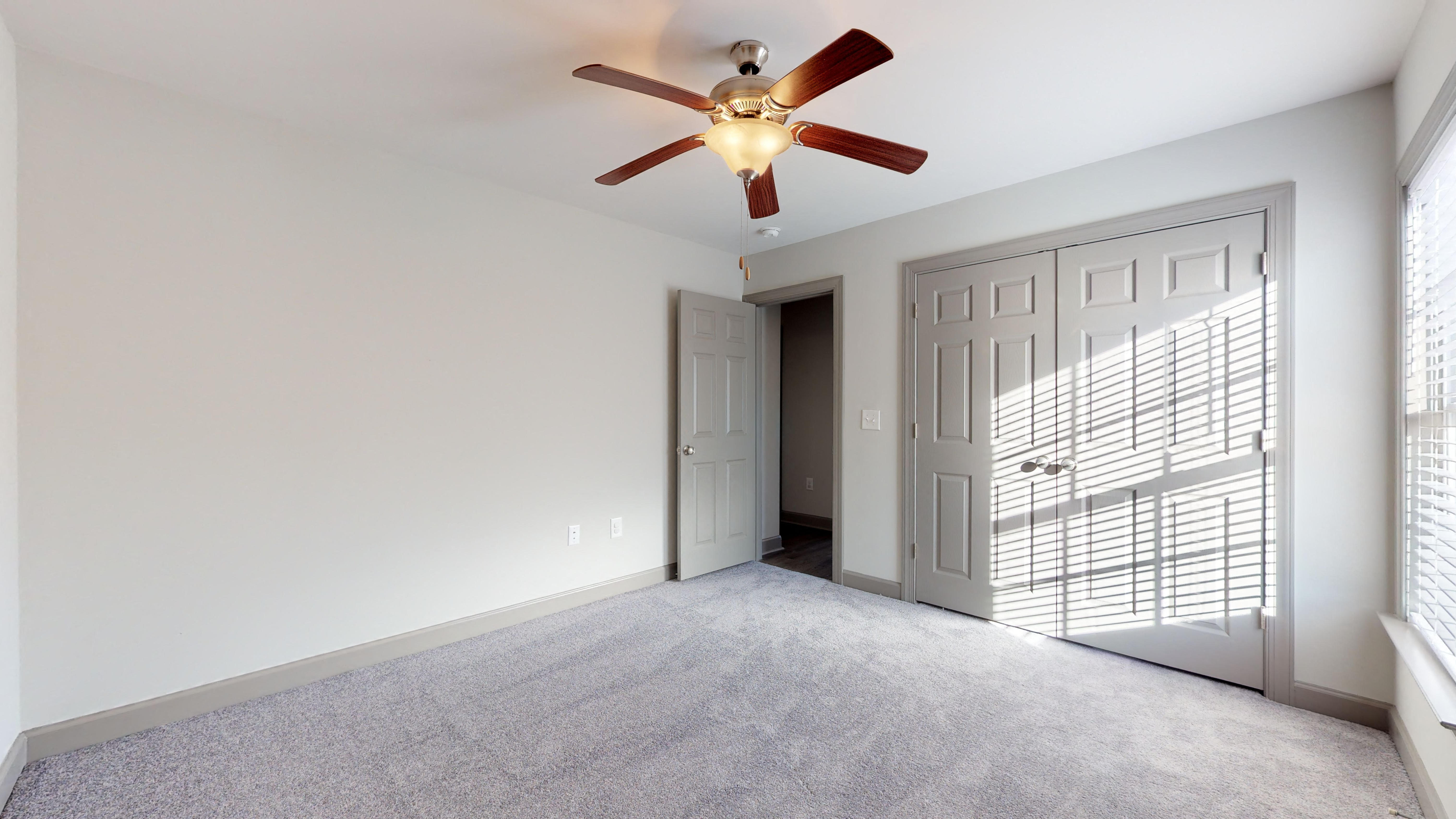 an empty living room with a ceiling fan and a door to a closet