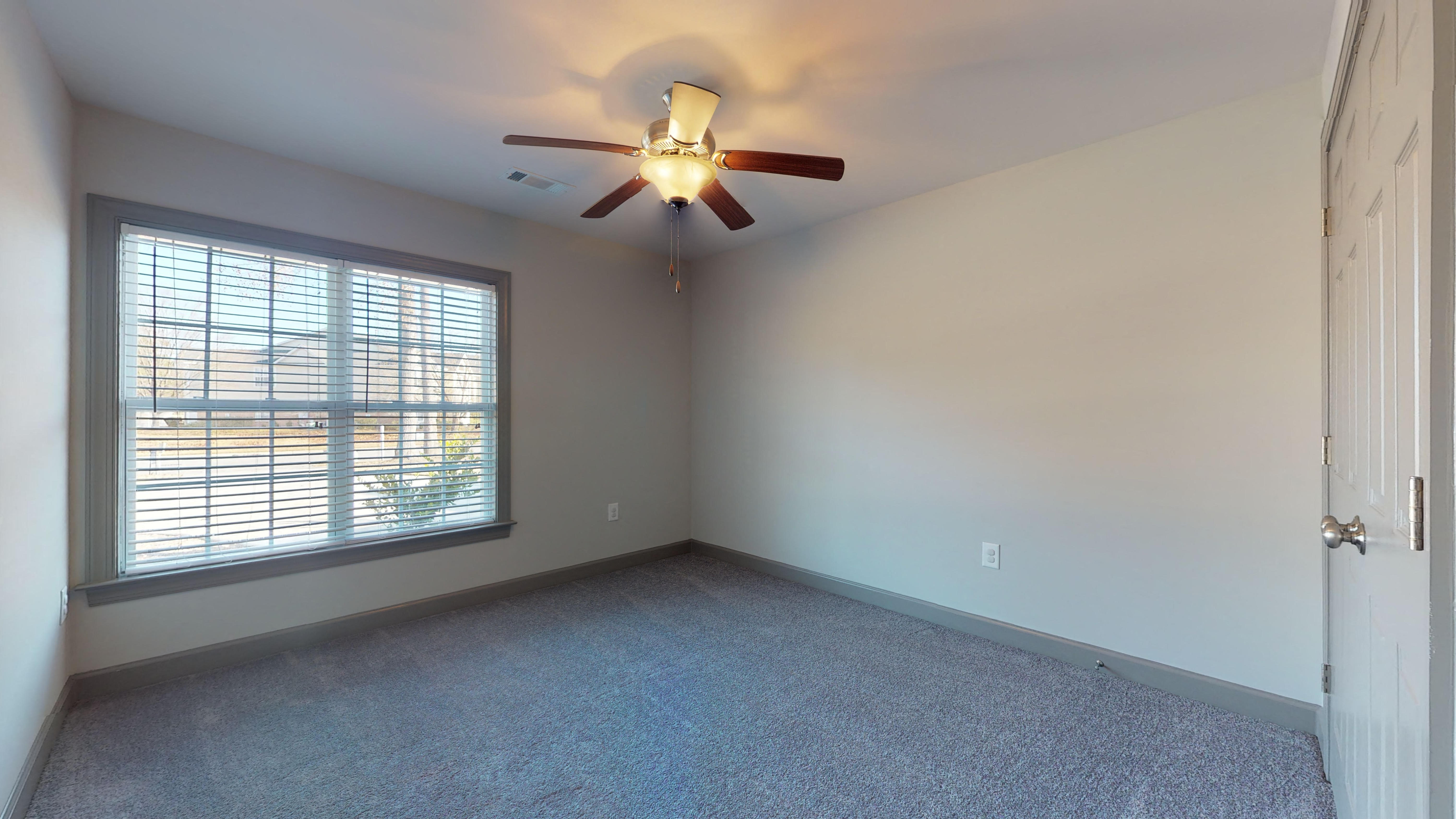 an empty bedroom with a ceiling fan and a window
