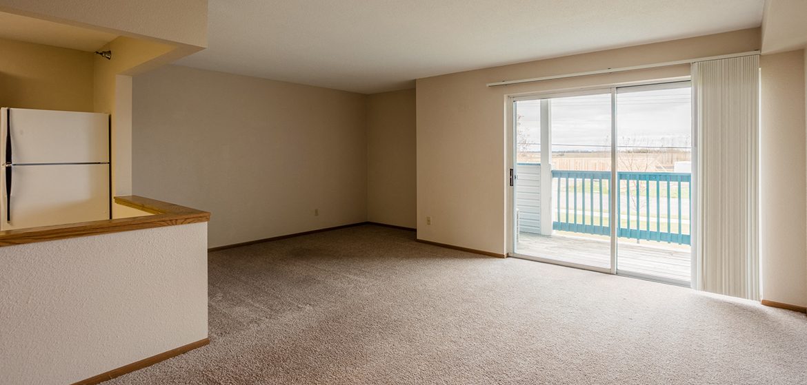 an empty living room with a sliding glass door to a balcony