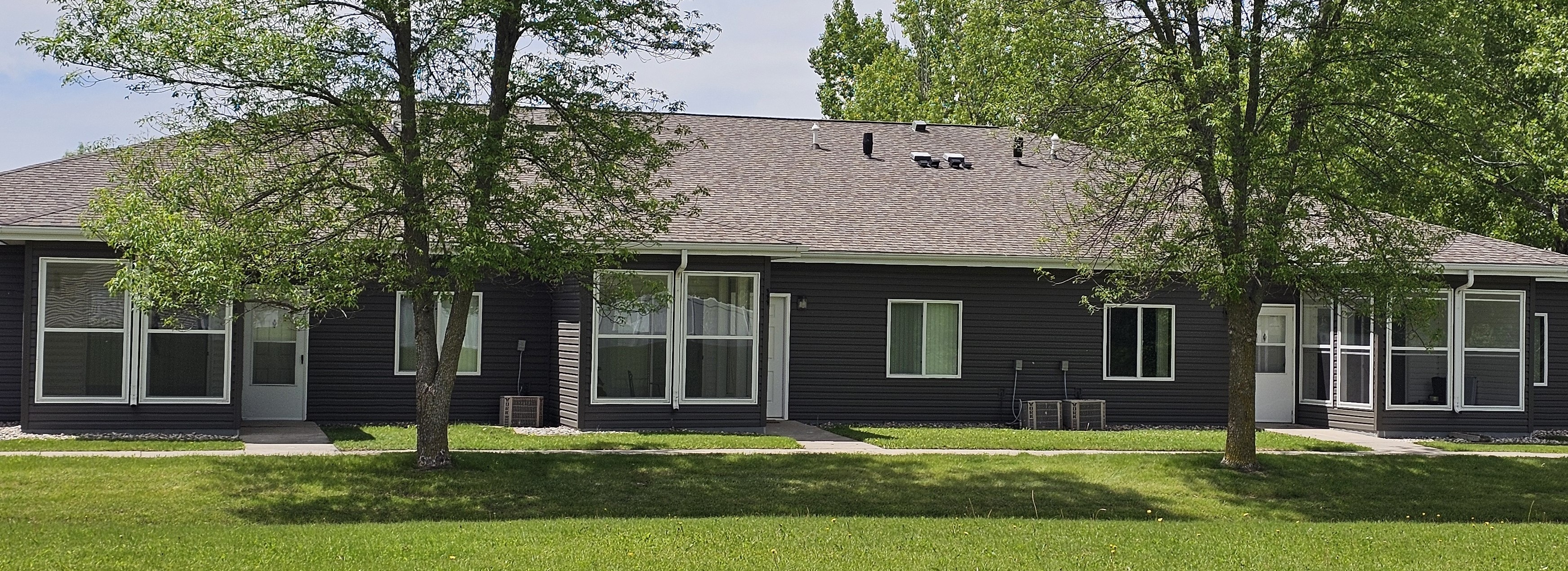 A house with a grey roof and green trees in front.