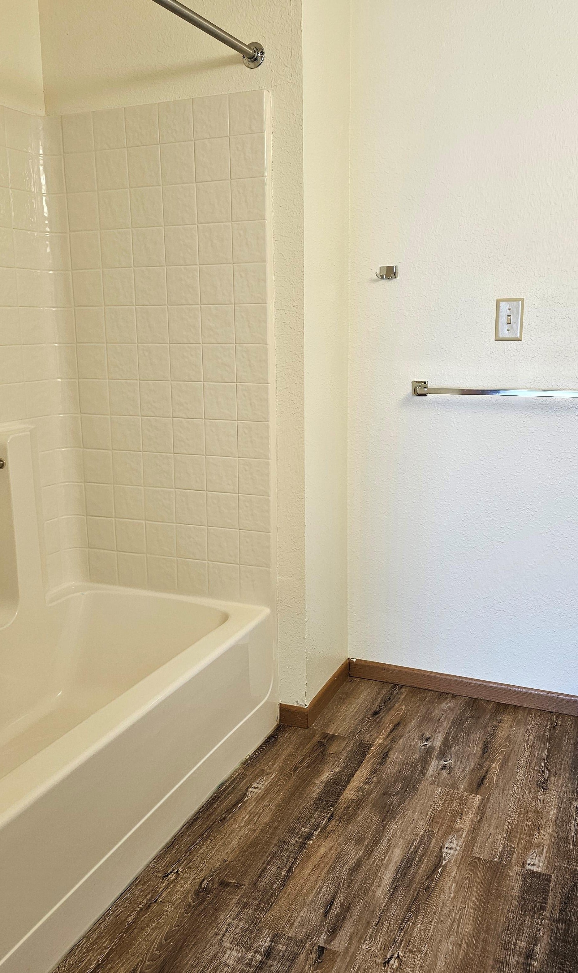 A white tiled shower area with a wooden floor.