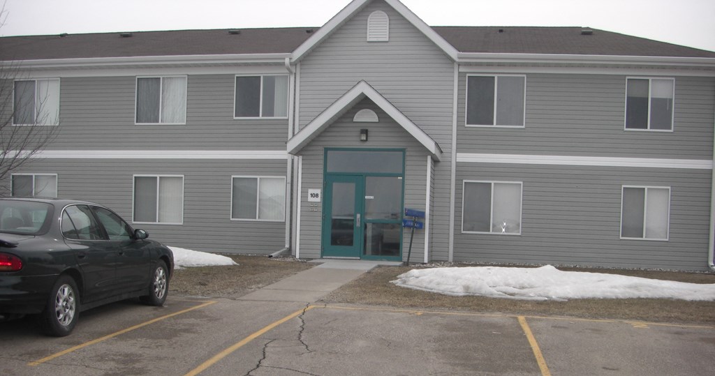 a gray building with a blue door and a car parked outside