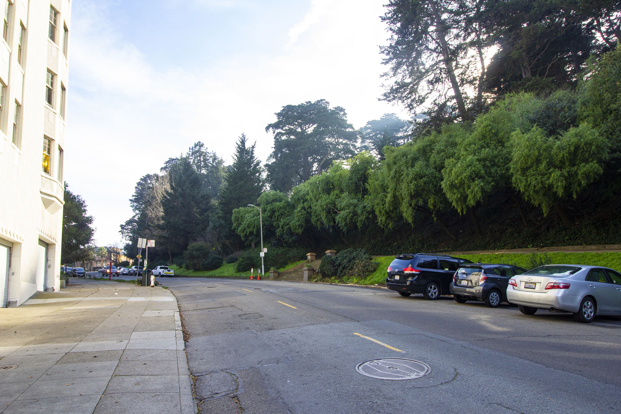 A street with cars parked on the side and a white building on the left.