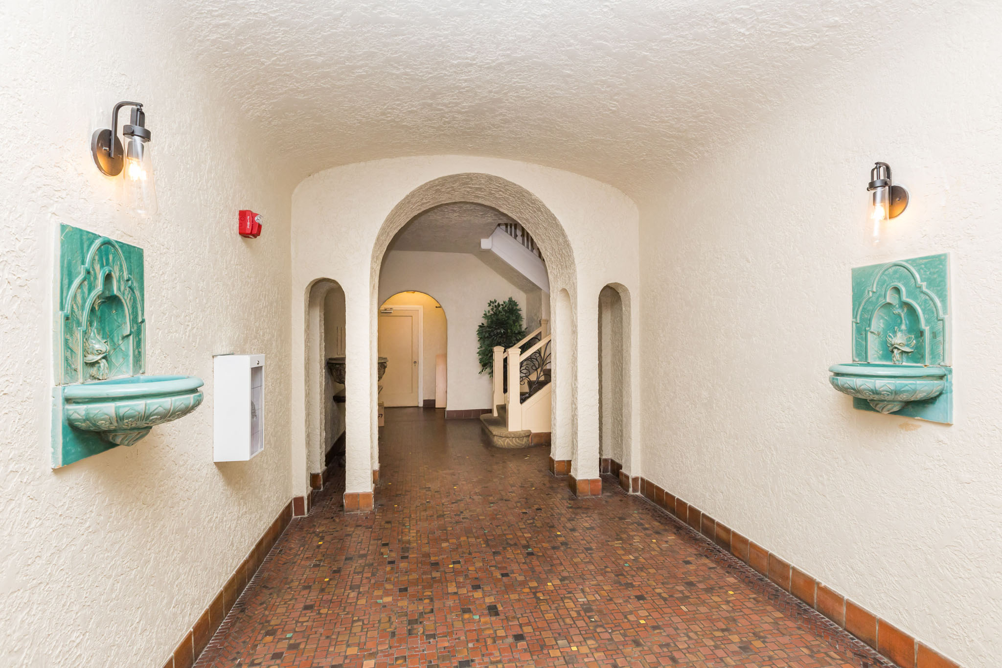 A long corridor with arches and a red fire alarm on the wall.