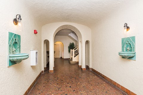 A long corridor with arches and a red fire alarm on the wall.